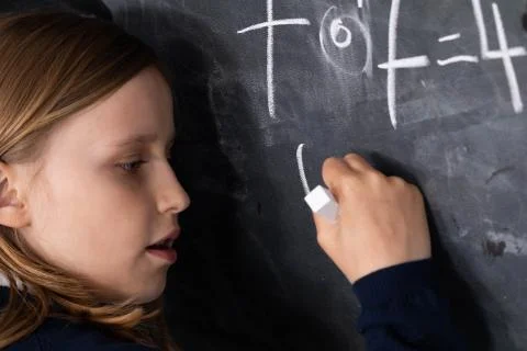 The student solves a math problem standing at the blackboard in her classroom Stock Photos
