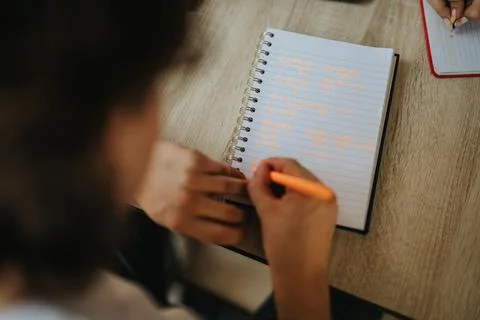 Student solving equations in notebook using orange pen during class Stock Photos