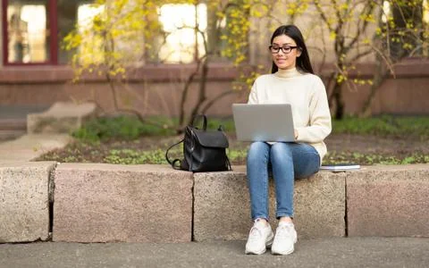 Student in specs using laptop, sitting on parapet 写真素材