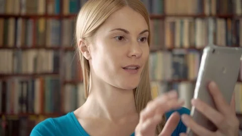 Student standing in library using her smartphone, chatting via messenger app Video stock 75334663
