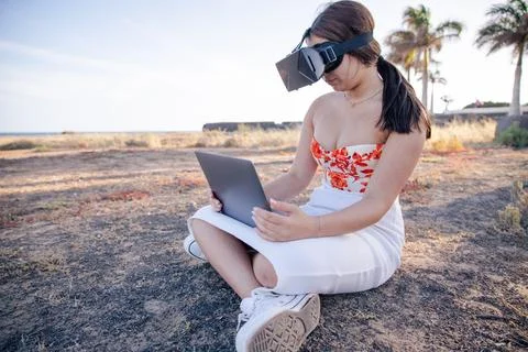 A student studies on the beach with a VR headset and her laptop Stock Photos