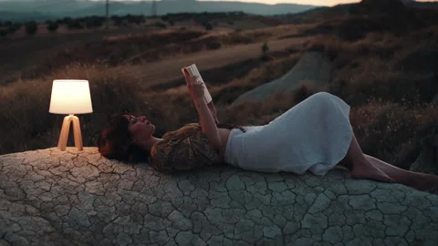 Student studies with a book on a rock at sunset Stock Footage 220501937
