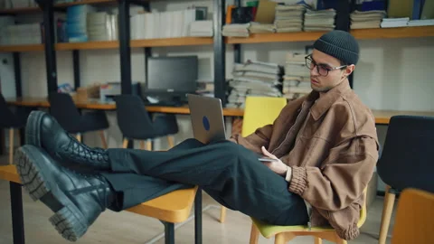 Student studies in a library using a laptop with books stacked on shelves nearby Stock Footage 337325060