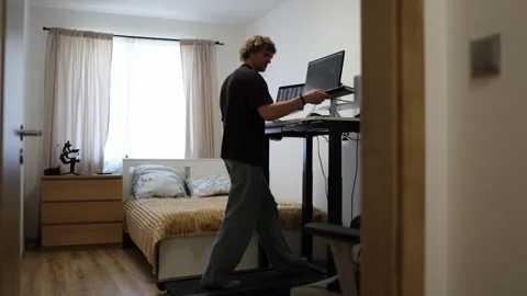 Student studies notes while walking on treadmill beside computer screens Stock Footage 346366051