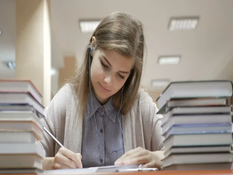 Student studying and taking notes in the library surrounded by books in college Free Stock Footage 82201520
