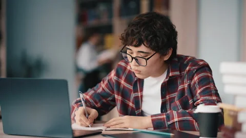 Student studying at desk with laptop and notebook wearing glasses Stock Footage 341888394