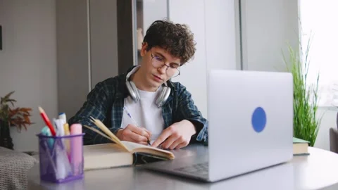Student studying at a desk with a laptop and notebook in a cozy room with plants Stock Footage 346185428