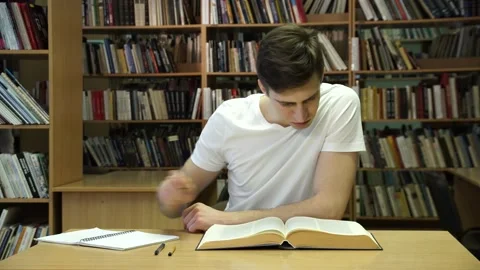 Student studying at a desk in the library on the background of books Stock Footage 155962929