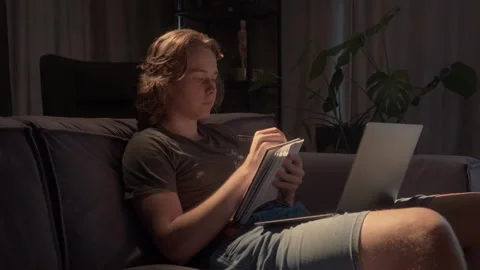 Student studying late at night, taking notes from a laptop in a dark room Stock Footage 310739272