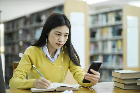 Student studying at library using phone. Stock Photos