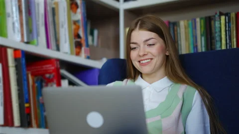 Student studying online and having video chat on laptop in library Stock Footage 163342873