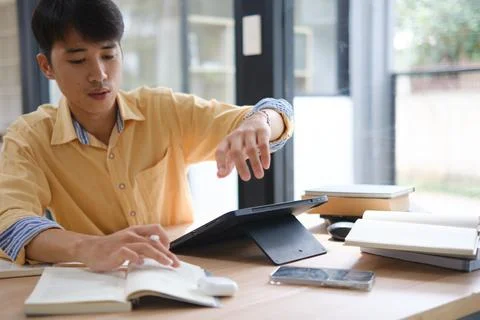 Student studying online and preparing for exams with digital devices and book Stock Photos