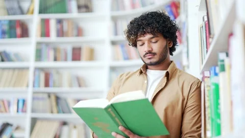 Student studying while reading a book while standing in campus library space Stock Footage 239735889