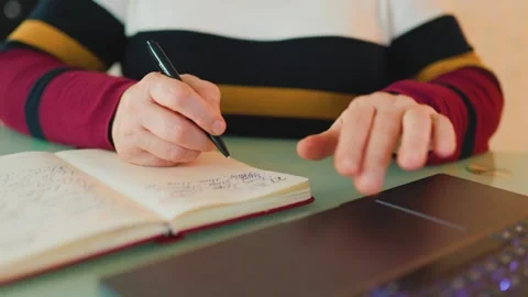 Student takes notes while studying at a desk with a laptop and notebook Stock Footage 304822597