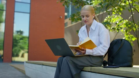 Student taking notes during online video class outdoors Stock Footage 318439492