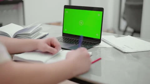 Student taking notes during an online class with a green screen laptop Stock Footage 327870842