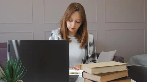 Student taking notes while studying on laptop at home Stock Footage 314647326