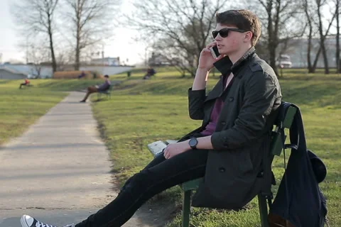 Student talking on cellphone in the park and sitting on bench Stock-Footage 48270627