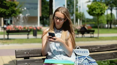 Student texting on smartphone and smiling to the camera on the bench Stock Footage 67378555