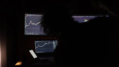 A student trading stocks from home using multiple monitors and a laptop in a dar Stock Footage 297112024