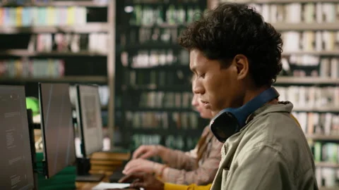 Student typing on keyboard beside open book at desktop computer lab Stock Footage 337230548