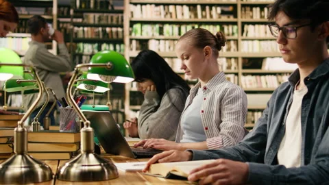 Student typing on laptop and taking notes from open book at library desk Stock Footage 336358591