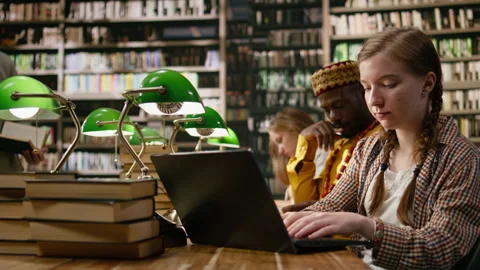 Student typing on laptop and taking notes beside open book at busy study table Stock Footage 337229153