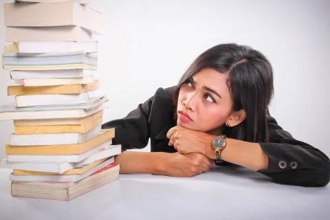Student under pressure, leaning down while looking up at pile of books Stock Photos