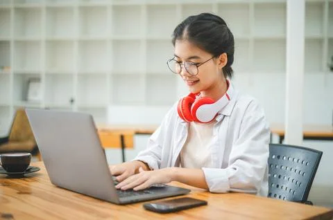 Student using a laptop in a cafe while wearing headphones, learning and sea.. Stock Photos
