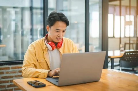 Student using a laptop in a cafe while wearing headphones, learning and sea.. Stock Photos