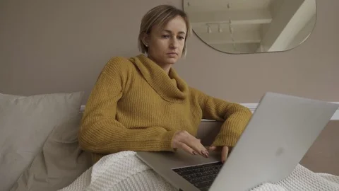 Student using laptop at home lying on sofa under blanket using computer serching Stockbeeldmateriaal 119524258