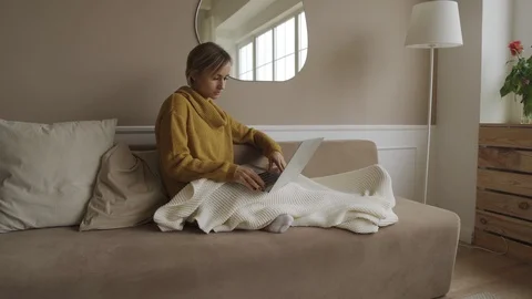 Student using laptop at home lying on sofa under blanket using computer serching Stock Footage 119524303