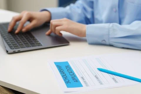 Student using laptop at white table, focus on scholarship application form .. Stock Photos