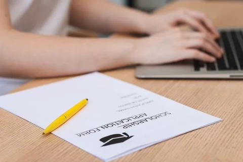 Student using laptop at wooden table, focus on scholarship application form.. Stock Photos