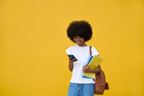 A student using phone in her hand and looking at her phone on yellow background Stock Photos