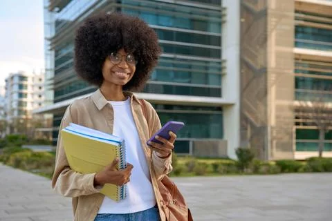 A student using phone in her hand and looking at camera on city background Stock Photos