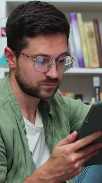 Student using tablet and writing notes in library for class assignment. Stock Photos