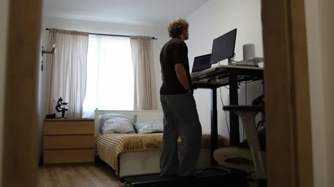Student walks on treadmill with hands in pockets watching online lessons at home Stock Footage 347269603