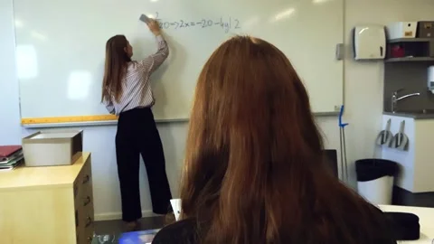 Student watching teacher erase math problems from whiteboard Stock Footage 346596328