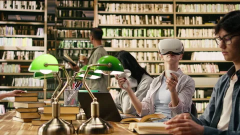 Student wears VR glasses and holds controllers in university library Stock Footage 336358813