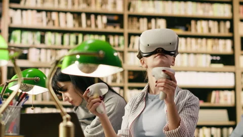 Student wears VR glasses and holds controllers in university library Stock Footage 336360491
