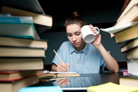 A student writes knowledge in a notebook and drinks coffee in the late evenin Stock Photos