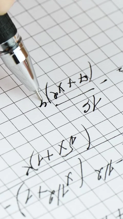 Student writes mathematical equations on graph paper. Close-up shot captures Видео 344999195