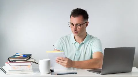 A student writes in a notebook - on the table books, textbooks, laptop Stock Photos