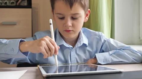 A student writes with a pencil on a tablet. a boy in a blue shirt is sitting at Stock Footage 167608841