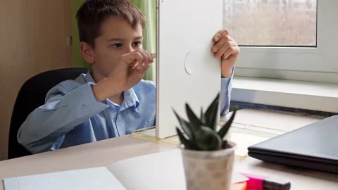 A student writes with a pencil on a tablet. a boy in a blue shirt is sitting at Stock Footage 168372713