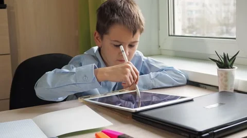 A student writes with a pencil on a tablet. a boy in a blue shirt is sitting at Stock Footage 171289152