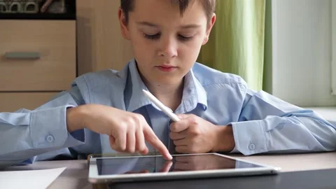 A student writes with a pencil on a tablet. a boy in a blue shirt is sitting at Stock Footage 171585785