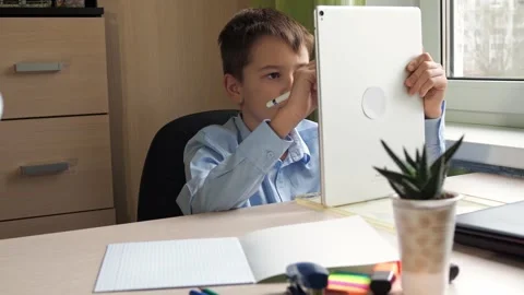 A student writes with a pencil on a tablet. a boy in a blue shirt is sitting at Stock Footage 172069946