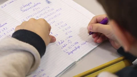 A student writing math problems in a notebook at a classroom desk, depictin.. Stock Footage 339861266
